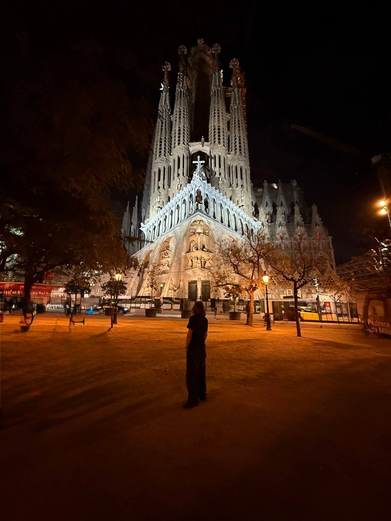 The Sagrada Família lit up at night, with Sinclair silhouetted in the square.