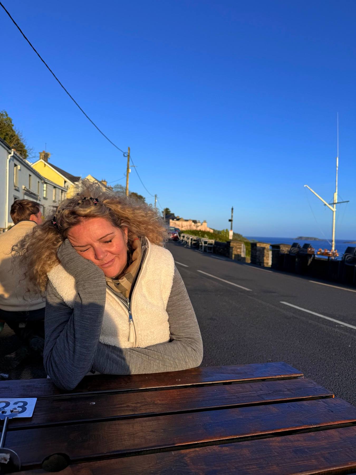 Carine sitting outdoors by the sea in warm evening light.