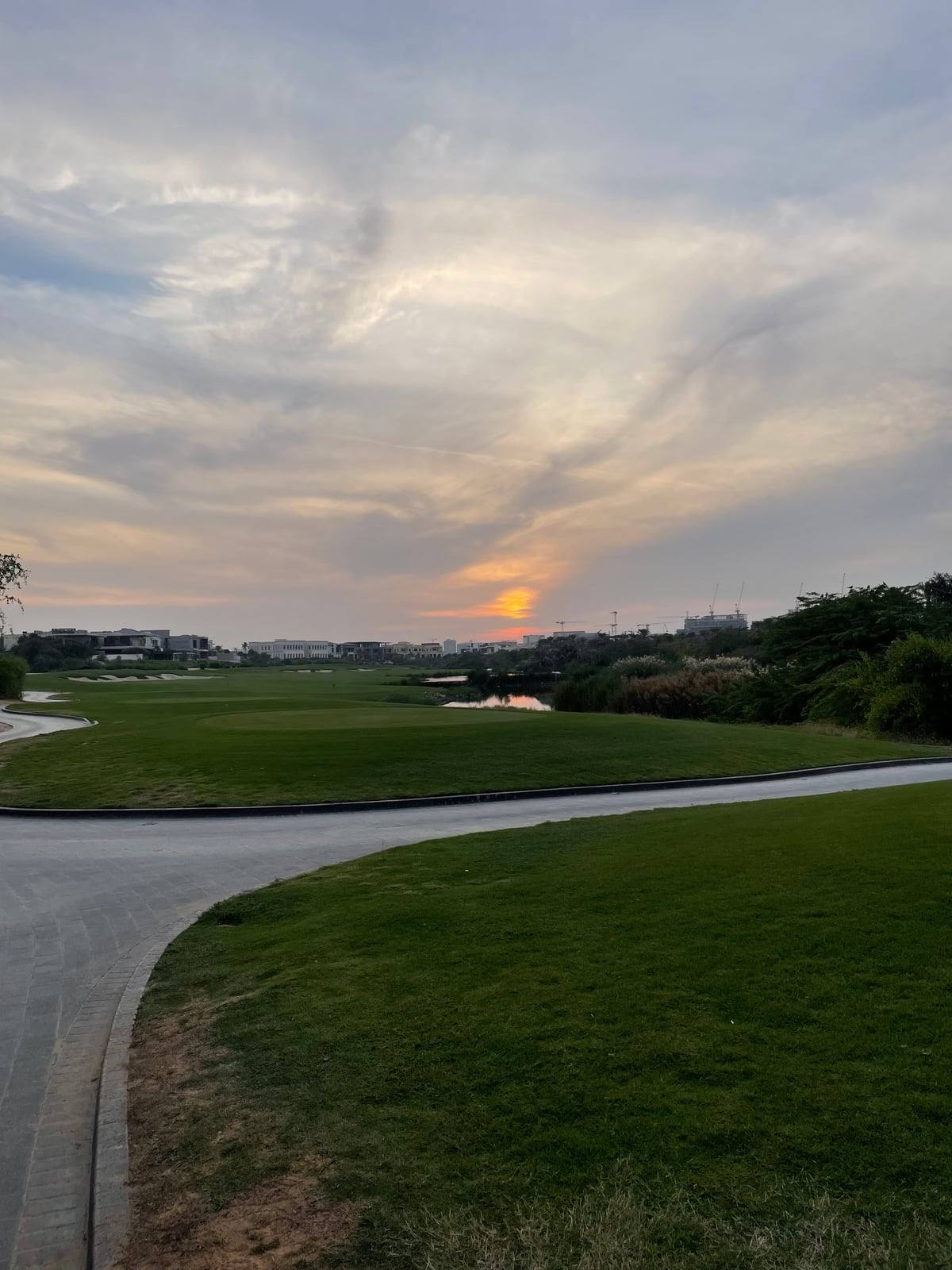 A golf course fairway at sunset, a path curving between the greens.