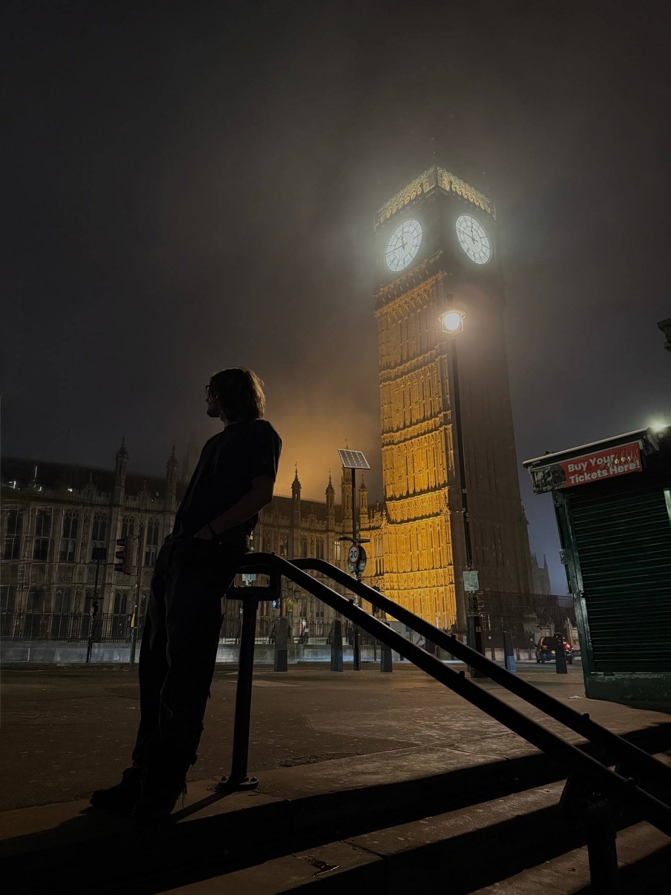 Big Ben glowing in fog at night, with Sinclair in silhouette on a stair rail.