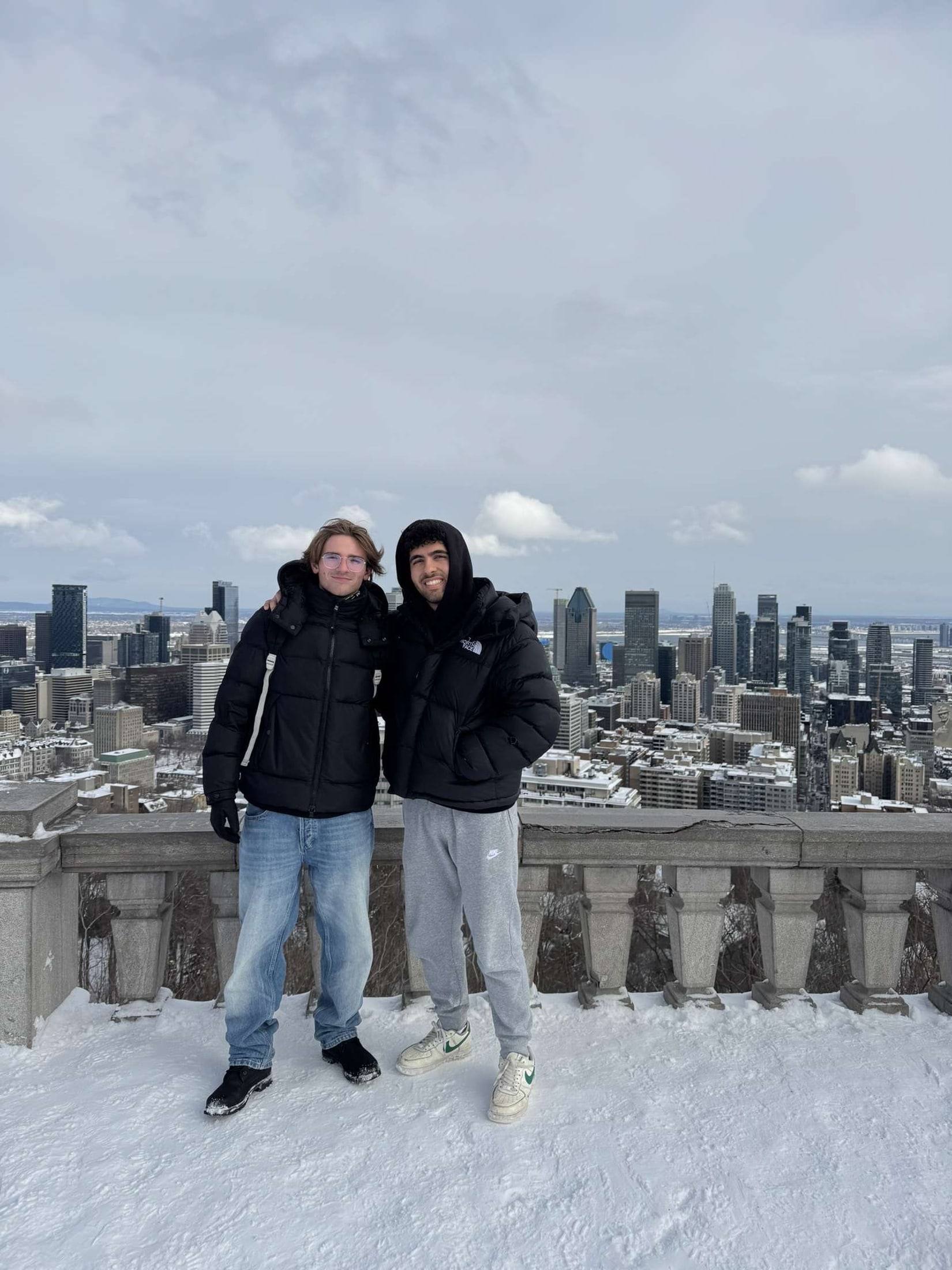 Sinclair and a friend in winter coats on a snowy lookout above the Montreal skyline.