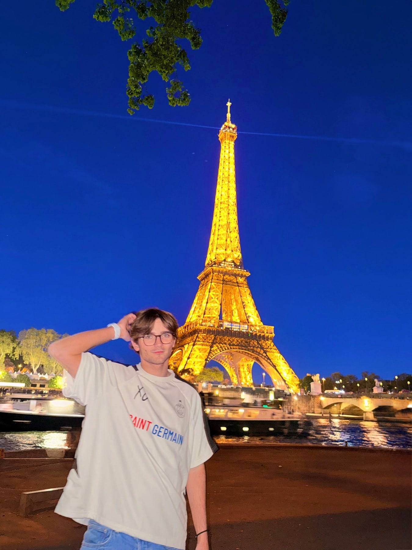 Sinclair in front of the Eiffel Tower lit gold at dusk.