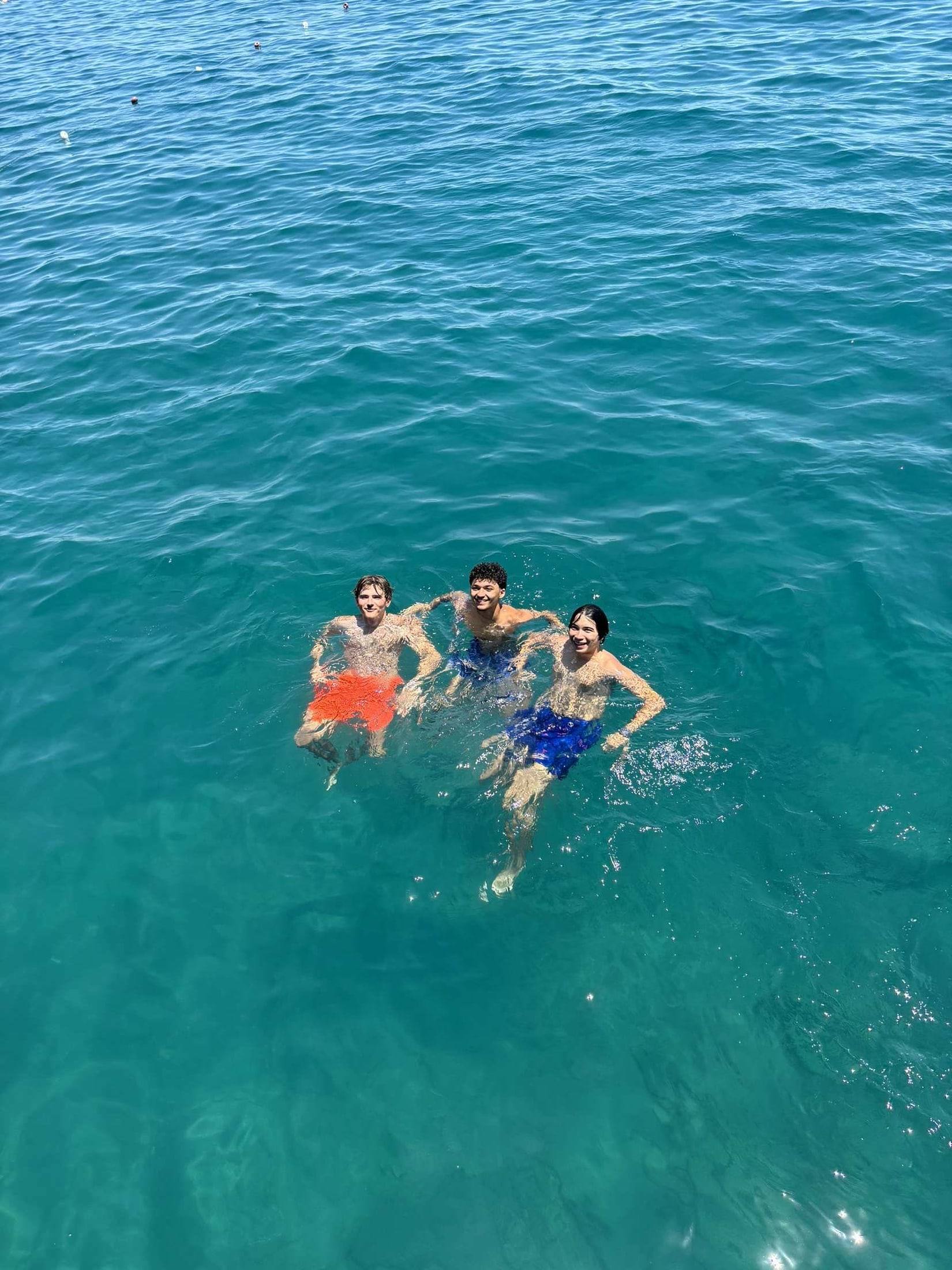 Three friends swimming in clear turquoise water, seen from above.