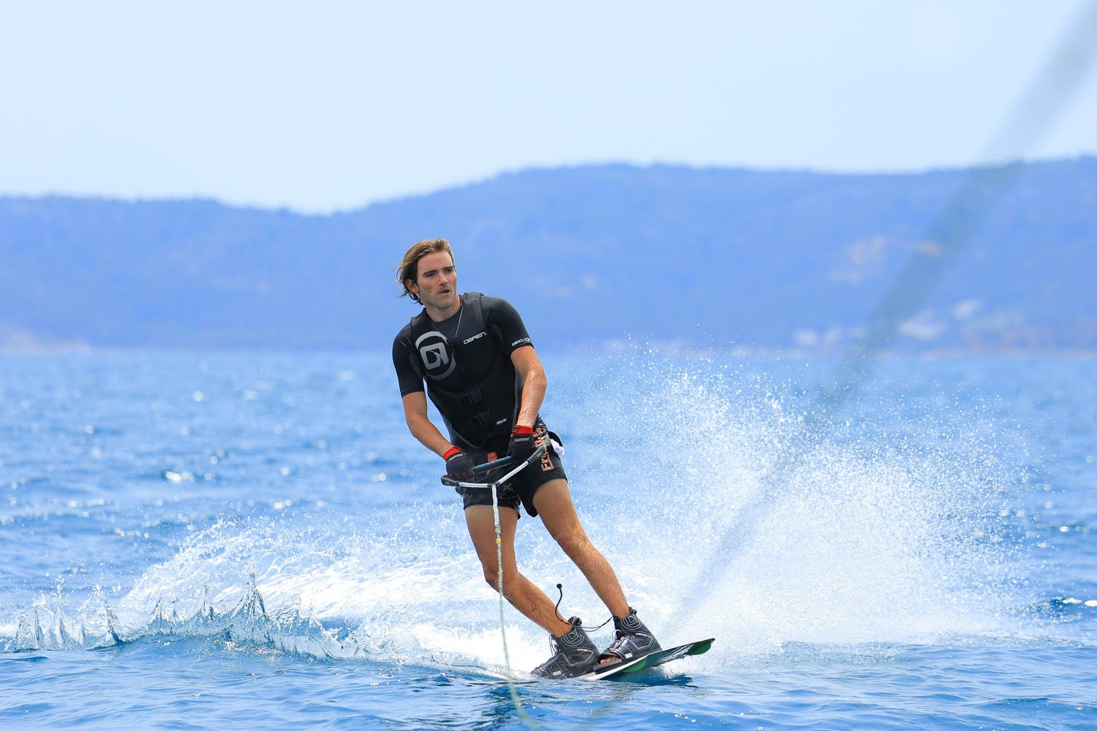 Sinclair wakeboarding across a lake, spray fanning out behind the board.